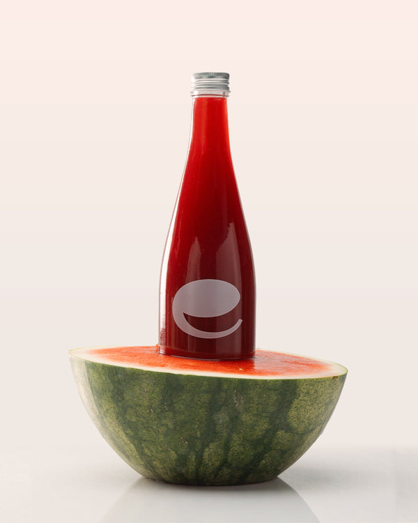 Bottle of red organic watermelon juice with eywa logo on top of a watermelon half against a white background